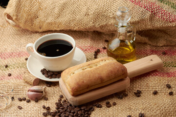 Obraz na płótnie Canvas Rustic bread placed on a cutting board, around it a cup of American-style coffee, olive oil, coffee beans and garlic, placed in a vegetable fiber sack