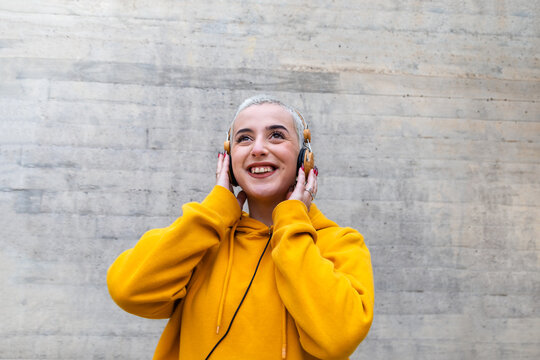 Gen Z Female Teenager With Platinum Blonde Buzz Cut Listening To Music With Wireless Headphones. Copy Space.