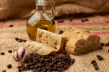 piece of rustic bread, around it coffee beans, olive oil, garlic, placed in a vegetable fiber sack