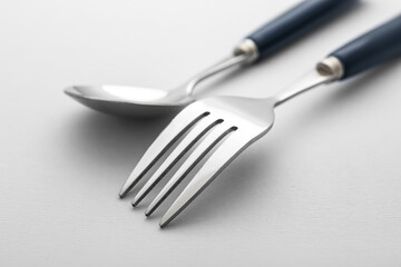 Stylish stainless steel fork and spoon on light background, closeup