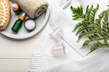 Vacuum jars for anti-cellulite massage, bathrobe and bath supplies on white wooden background