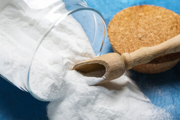 Jar with baking soda and scoop on blue background, closeup