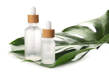 Bottles of natural serum and palm leaf on white background, closeup