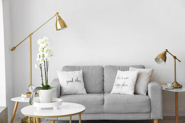 Table with orchid flower and comfortable sofa near white wall