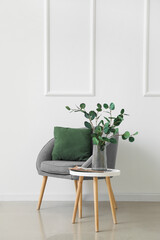 Table with eucalyptus in vase, magazine and armchair near light wall