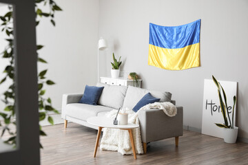 Interior of light living room with hanging Ukrainian flag, sofa and houseplants