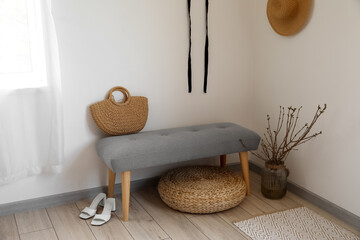 Soft bench with bag, tree branches in vase, pouf and shoes near light wall