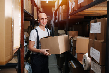 Cheerful male warehouse worker holding a box, radiantly smiling
