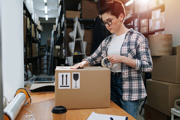 Focused short haired female warehouse worker packing a cardboard box