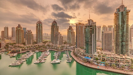 Sunrise over Dubai Marina luxury tourist district with skyscrapers and towers around canal aerial timelapse