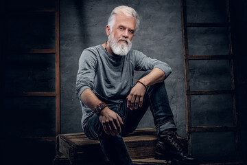 Shot of fashionable aged man dressed in gray shirt with wooden ladder sitting on firewood.