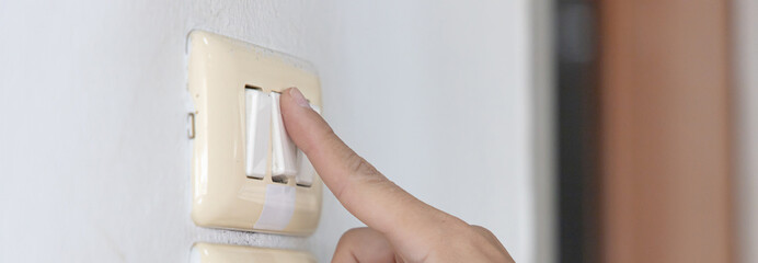 Naklejka premium Close up young man's hand pressed the button to turn on the light switch, Open the electrical circuit beside the wall.