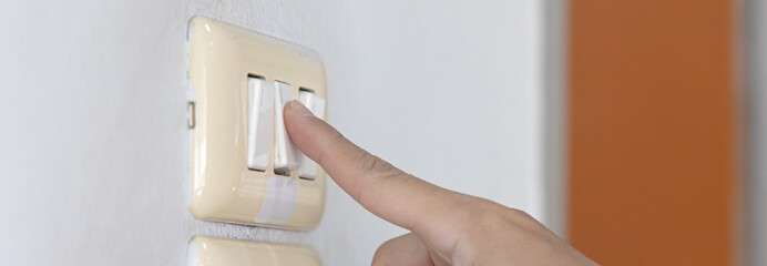 Close up young man's hand pressed the button to turn on the light switch, Open the electrical circuit beside the wall.