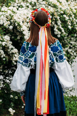 The girl stands with her back in Ukrainian national clothes and a wreath with ribbons on her head. - 507740808