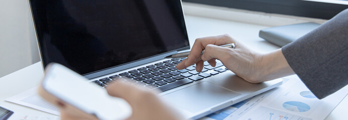 Finance workers are reviewing the company's financial data on a laptop and using smartphones to...