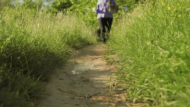 Earth Day. A young pretty woman running at the park and collects garbage. Low angle view. Follow shot. The concept of plogging and volunteering.
