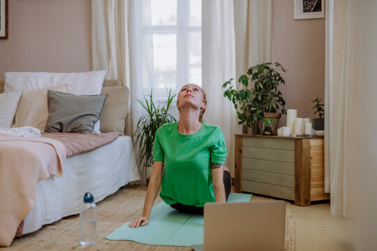 Woman practicing yoga e-learning through laptop at home