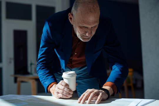 Businessman holding disposable cup checking time on smart watch at desk