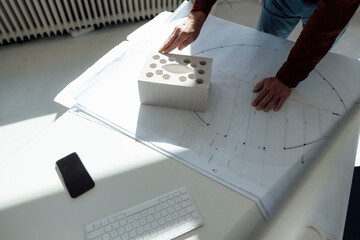 Hands of architect on concrete brick and blueprint at desk