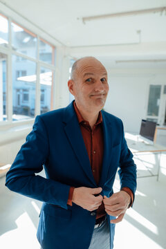 Smiling businessman buttoning blazer in office