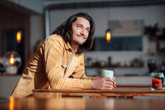 Happy man with coffee cup leaning on table at coffee shop