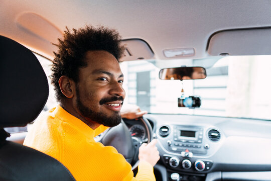 Smiling Afro man driving car looking over shoulder
