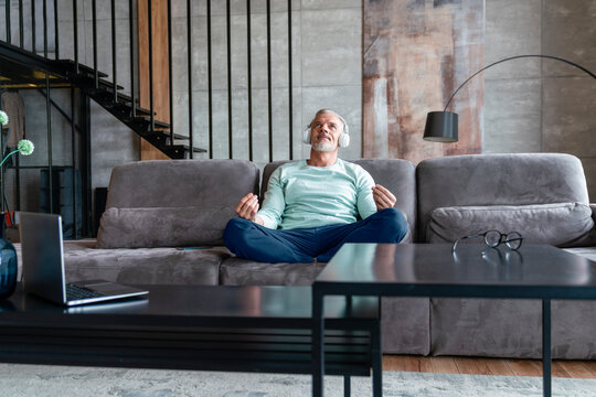 Man listening music through wireless headphones mediating on sofa at home