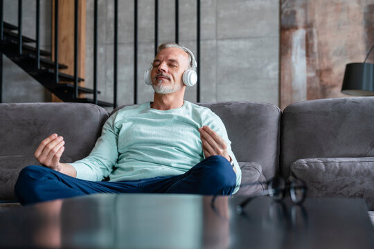 Man listening music through wireless headphones mediating on sofa