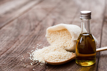 Sesame oil in glass bottle with white sesame seeds in sack bag isolated on wooden table background. 
