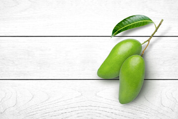 Green mango fruit with green leaf isolated on white wooden table background. Top view. Flat lay.