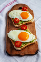 Homemade Healthy Egg, Avocado and Tomato Toast on a rustic wooden board, side view.