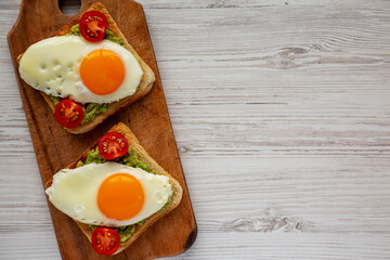 Homemade Healthy Egg, Avocado and Tomato Toast on a rustic wooden board on a white wooden background, top view. Flat lay, overhead, from above. Copy space.
