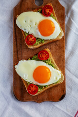 Homemade Healthy Egg, Avocado and Tomato Toast on a rustic wooden board, top view. Flat lay,...