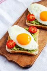 Homemade Healthy Egg, Avocado and Tomato Toast on a rustic wooden board, side view.  Close-up.
