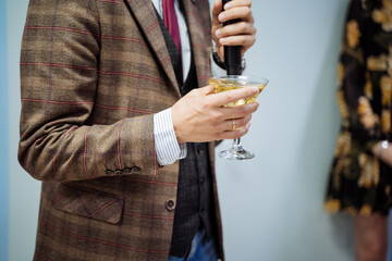 A person's hand holds a glass of wine, gives a speech at a speech, drinks champagne at parties, an engagement ring, a plaid jacket, a shirt sleeve sticks out.