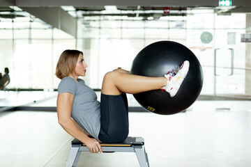 A young woman does abs exercises in the gym on a bench using a fitball. The concept of sports and a healthy lifestyle