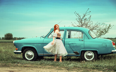 Red-haired girl in a retro dress next to a 1965 vintage car