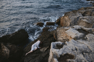 beautiful young woman lying on rocky coast with cracks on rocky surface unaltered