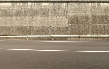 Metalllic guard rail before a rough high concrete wall. Two lane asphalt road in front Background for copy space.