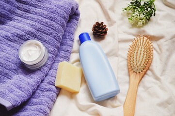 Flat lay object photography. Beauty still life image. Purple towel, moisturizing cream jar, natural soap, blue shampoo bottle, wooden hairbrush. Top view bath products