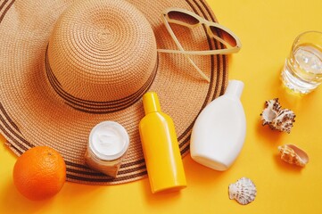 Summer travel accessories and cosmetics for women. Straw hat, moisturizing cream, sunscreen lotion, shampoo, sunglasses on a yellow background