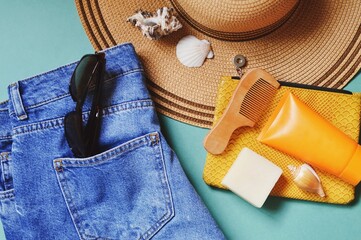 Summer travel lifestyle flat lay photography. Trendy jeans, straw hat, yellow cosmetic bag, sunscreen cream, solid shampoo, wooden comb