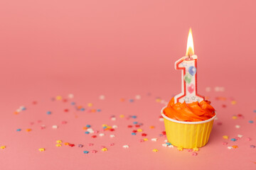 Number 1 candle in a cupcake against a pastel pink background. First bithday cake