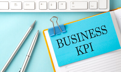 BUSINESS KPI text on sticker on the blue background with pen and keyboard