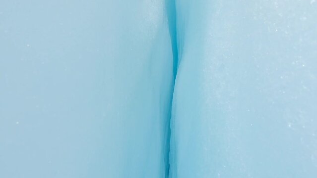 Closeup into a small crevasse with deep blue and white ice tilting the camera upwards reveilling the beauty of New Zealands Franz Josef Glacier surrounded in a grey rocky landscape