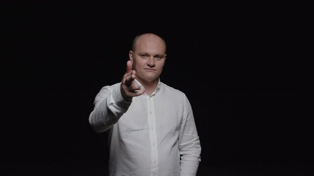 An elegant bald man in a white shirt shoots his fingers and poses for the camera on a black background.