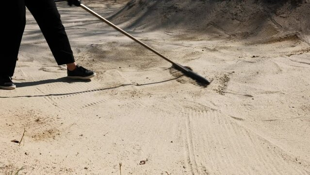 Golfer Raking the Sand Trap on Golf Course in a Sunny Day in Switzerland.