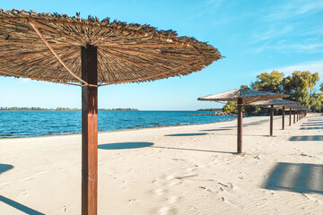 Straw beach umbrellas for shade near the river on the background of the landscape.