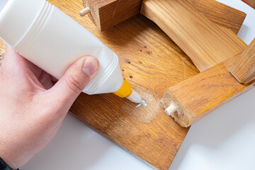 Do-it-yourself home furniture repair, giving old things new life concept image. Person's hands applying white glue on broken wooden furniture.