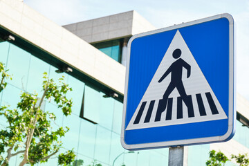 blue square crosswalk traffic sign with glass building in the background